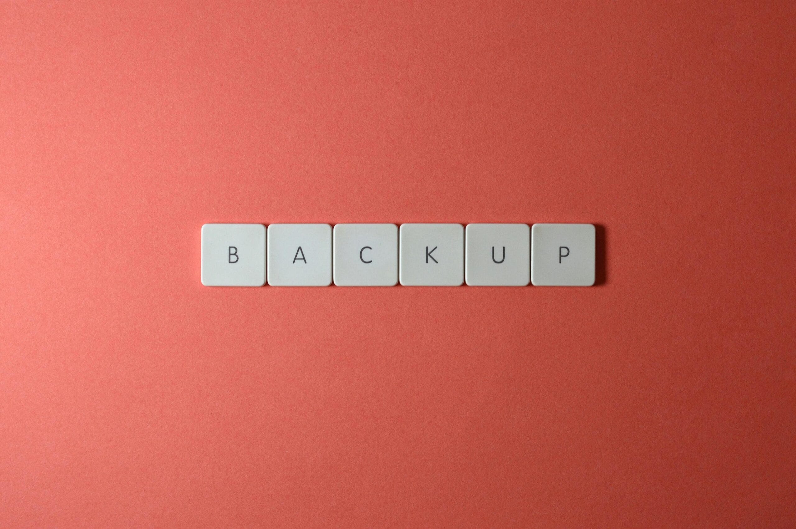 Free Close-up of keyboard keys spelling 'BACKUP' placed on a coral-colored surface. Stock Photo